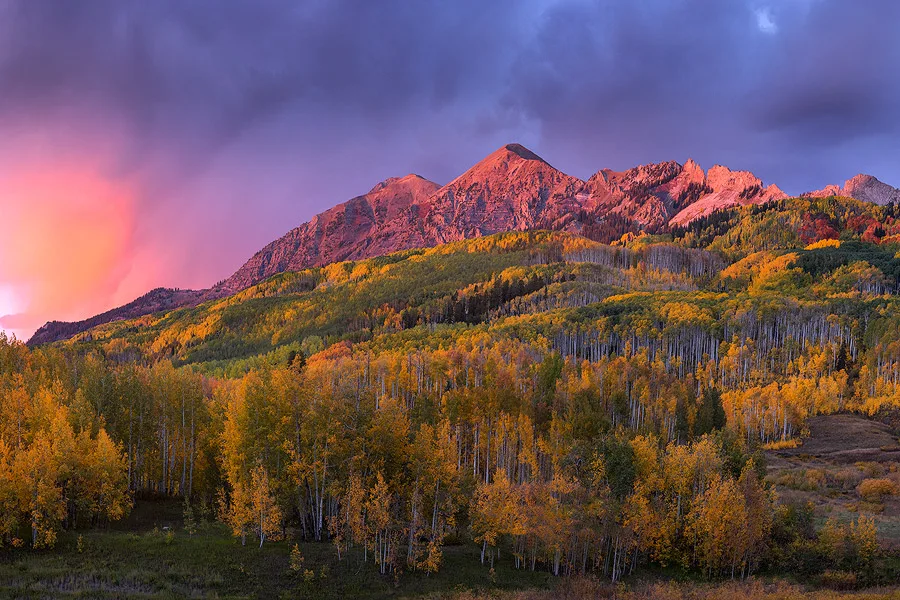 The sky explodes with red and casts alpenglow along the mountain ridges during peak falls colors in Colorado during our photography workshop.