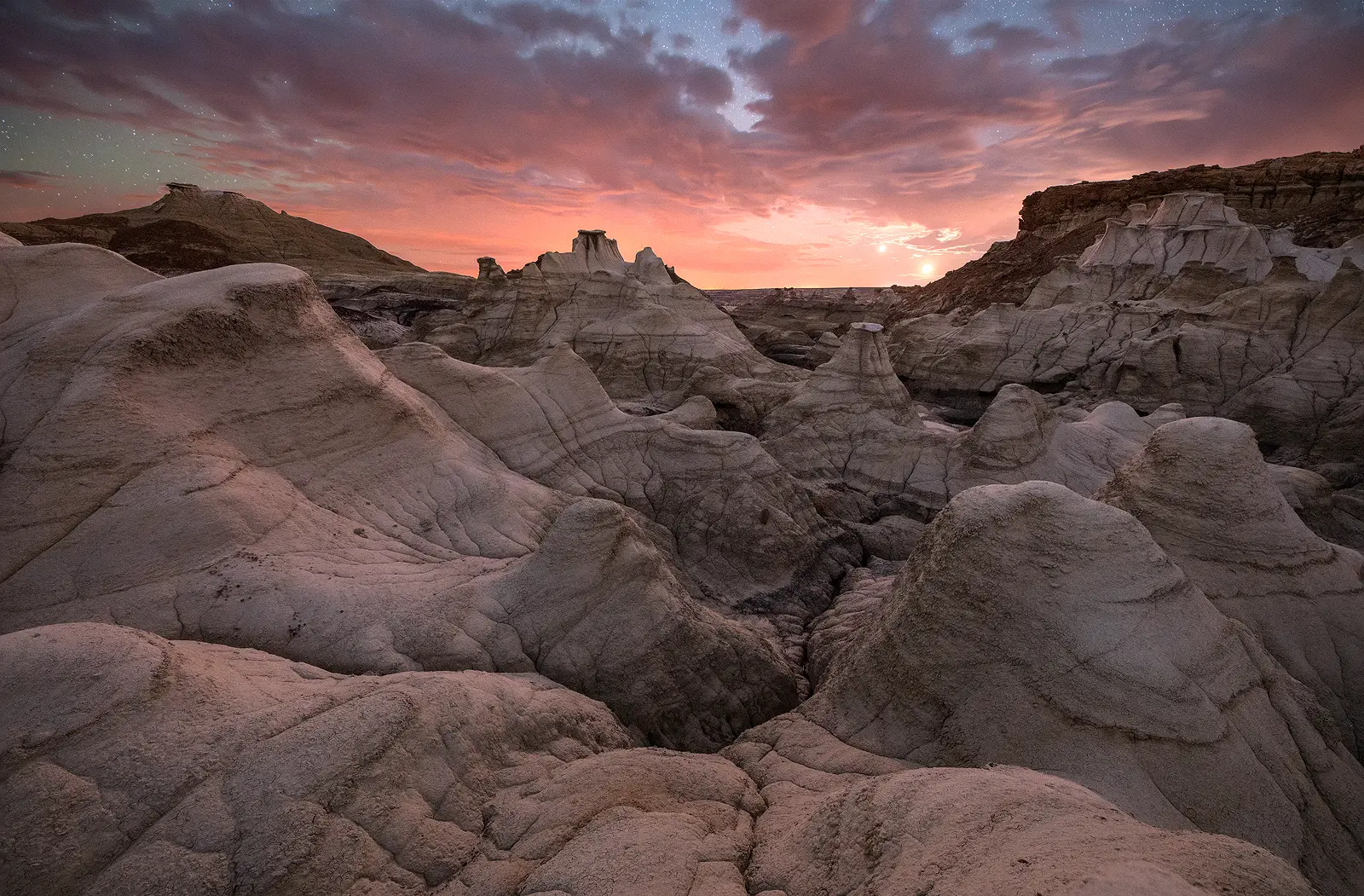 The moon and Venus set in a pastel pink and purple twilight sky over the eroded hoodoos and formations of the Bisti Badlands in New Mexico