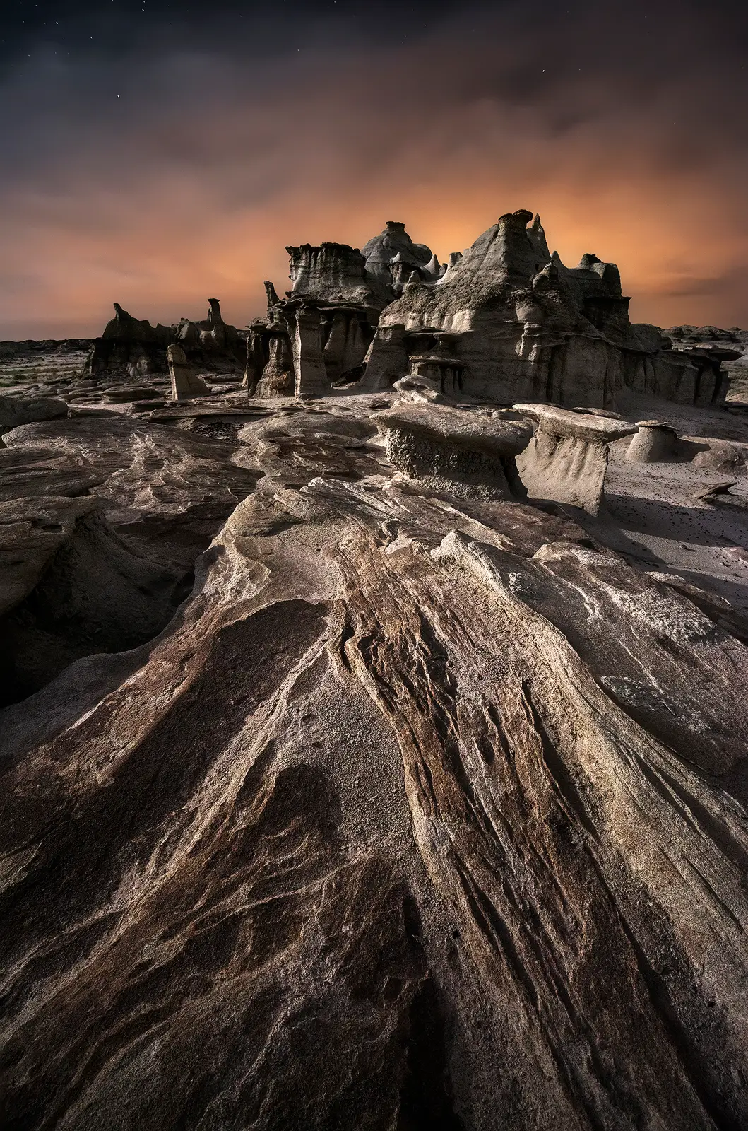 Moonlight illuminates eroded hoodoos and layered rock formations in the Bisti Wilderness of New Mexico under a cloudy night sky