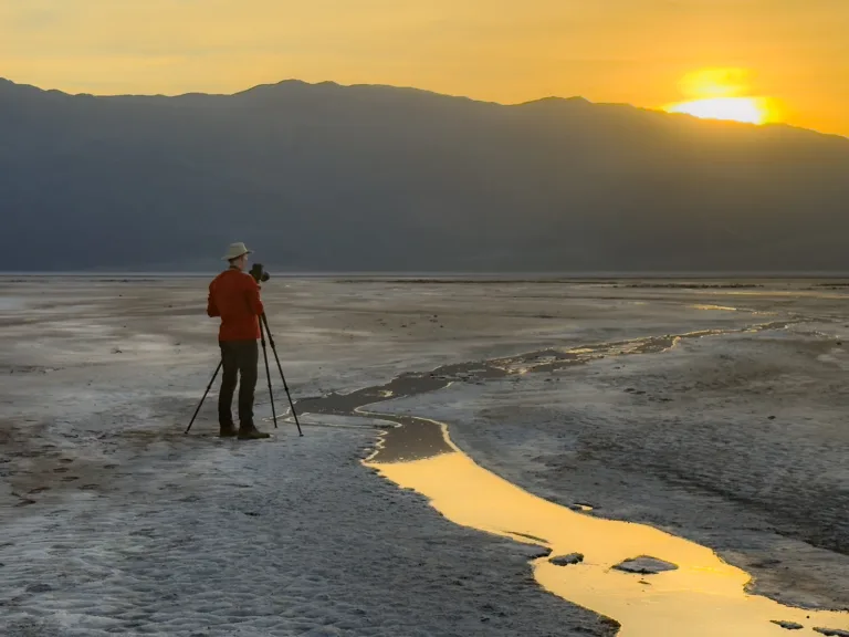 A night photography workshop participant in shooting a golden sunset reflected in a winding water channel across the salt flats.