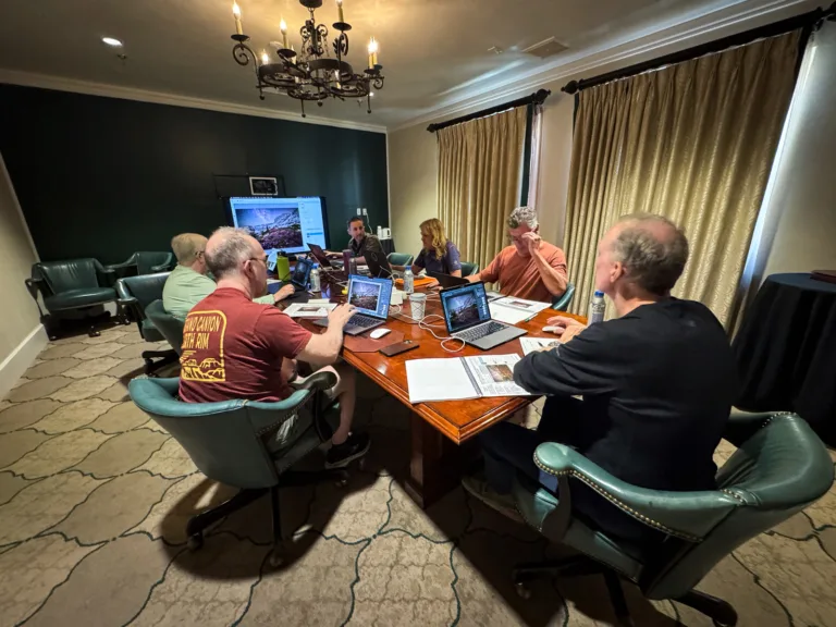 Brad Goldpaint teaches his post processing approach to night photography workshop participants reviewing and editing photos on laptops around a table during an indoor classroom session.
