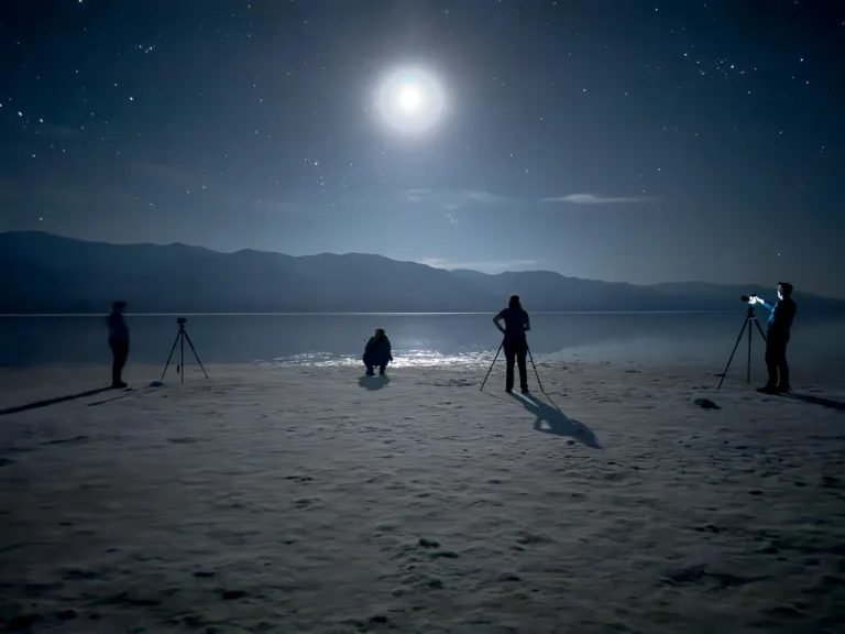 Silhouetted night photography workshop participants shooting under a bright moon and stars on the Death Valley salt flats.