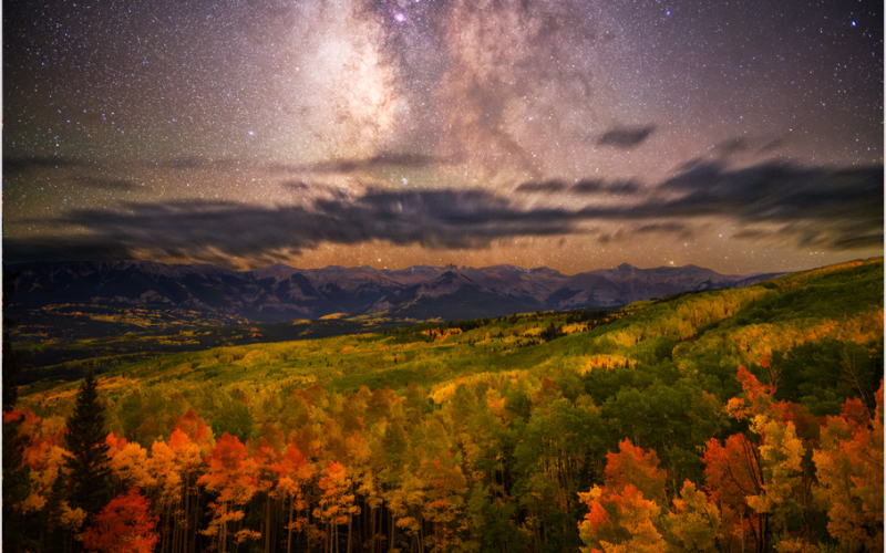 The Milky Way hovers above peak fall colors that create a blanket of explosive hues across the aspen groves of Gunnison National Forest.